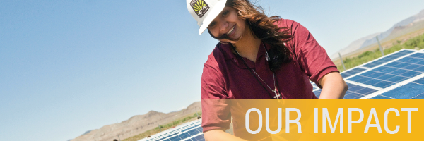 Female solar installer with long brown hair standing in front of solar panels. Our Impact words in lower right corner.