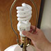 Photo of compact fluorescent light bulb being installed into lamp.